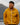 Smiling youth wearing a heather mustard Campfire Nights full zip hoodie with Rock Life logo, standing outdoors with mountains in the background, cozy camping apparel