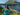 Woman wearing Rock Life teal tank top on grassy hillside overlooking blue lake and mountains in Kodiak, Alaska – island life apparel and adventure gear