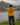 Back view of youth standing with arms raised in heather mustard Campfire Nights full zip hoodie featuring campfire and mountain design, outdoors by lake and peaks, camping lifestyle hoodie