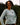 Smiling woman wearing Campfire Nights long sleeve tee with Rock Life mountain logo on chest, standing in forest setting, cozy outdoor shirt for camping and hiking