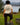 Back view of woman outdoors by ocean wearing heather natural Campfire Nights short sleeve tee with mountain and campfire graphic, casual camping and hiking apparel
